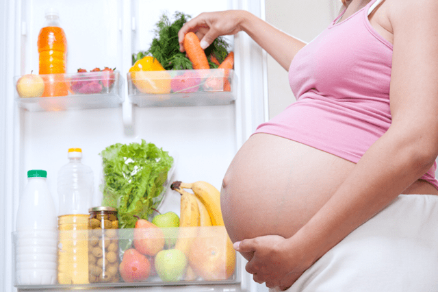 embarazada tomando verduras del refrigerador
