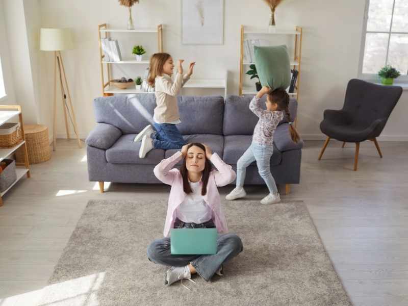 Mamá multitarea en sala de estar mientras cuida a sus hijos y organiza pendientes